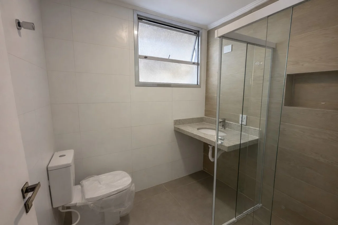 Banheiro da suíte reformado, com box blindex, revestimentos novos e nicho no chuveiro